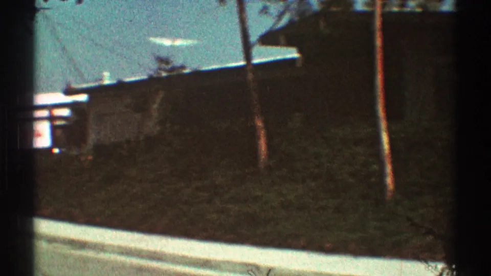 1969 Los Angeles suburban view with a grassy slope, curb, trees, utility pole, and low residential buildings.