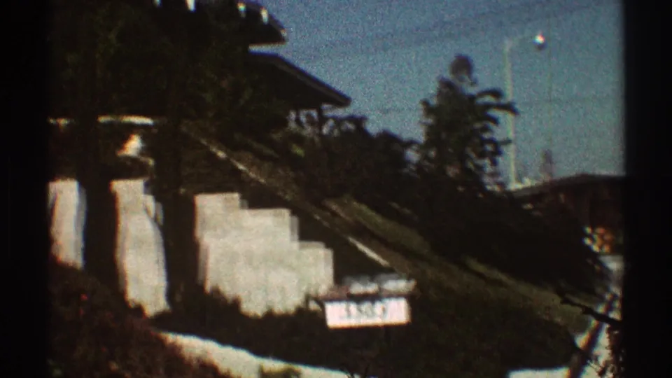 1969 Los Angeles frame showing a stucco house exterior with steps, a sloped yard, trees, and a visible house number sign.