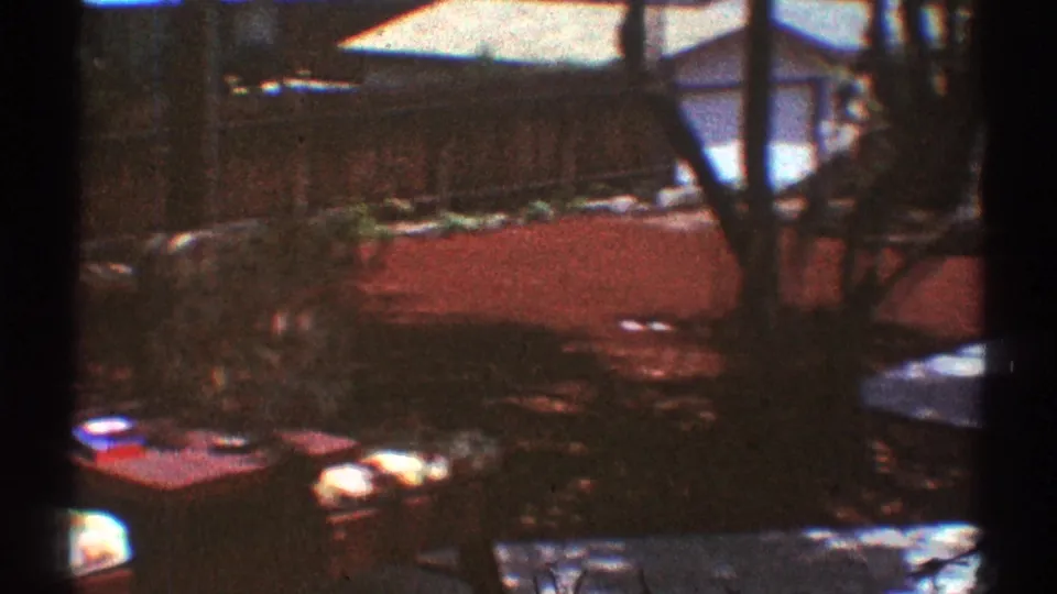 Suburban Los Angeles backyard with low outdoor tables, scattered small items, a fence, plants, and a red-covered yard area.