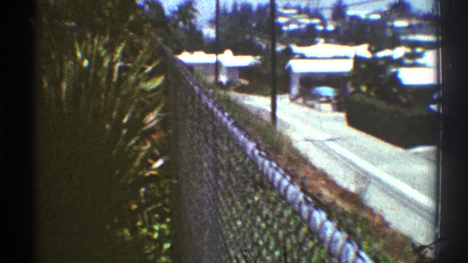 1969 Los Angeles home-movie view looking down past a chain-link fence toward a residential street and rooftops.