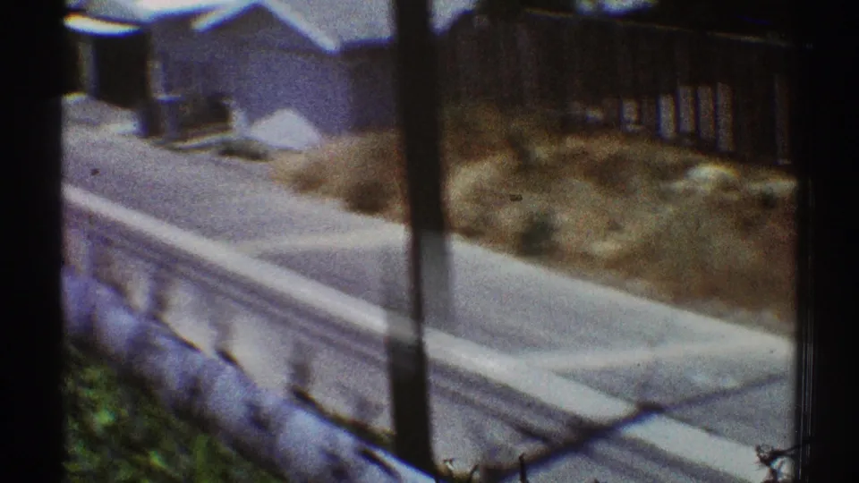 1969 Los Angeles frame showing a sidewalk, low wall, dry yard planting, and nearby residential rooflines.