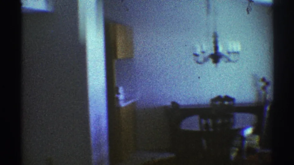 Shadowed Los Angeles apartment dining area with chandelier, table, chairs, and a partial wall in blue-tinted 8mm footage.
