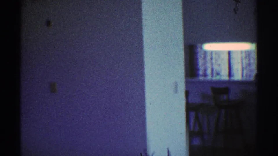 Blue-tinted 8mm view of a Los Angeles apartment kitchen counter with bar stools, partly obscured by an interior wall.