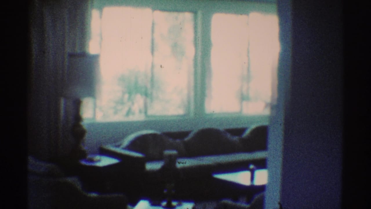 Dim living room with bright windows, sofa, table, and lamp in soft focus.