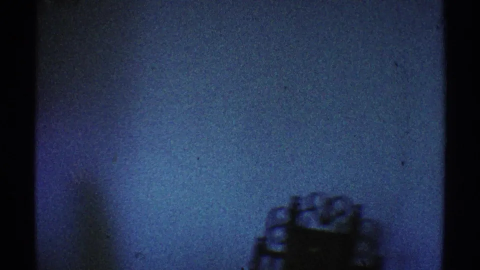 Blue-green 8mm frame of a mostly bare interior wall with a small decorative object or furnishing partly visible at right.