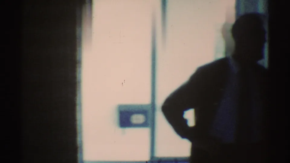 Backlit 1969 home interior with a bright glass door or window, curtains, and a dark foreground shape in soft focus.
