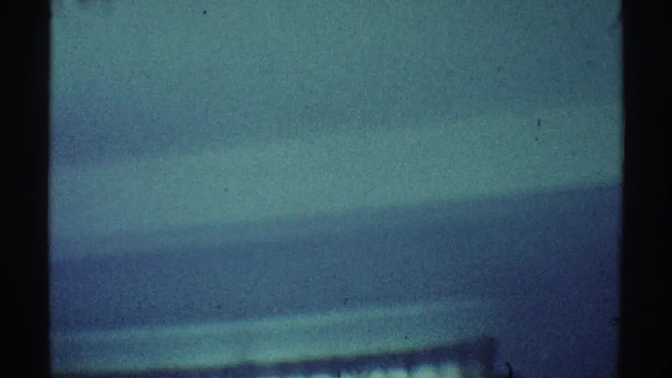1969 Los Angeles home-movie frame showing a teal interior wall, dark vertical framing, and soft diagonal shadows.