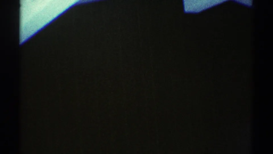 Dim 1969 Los Angeles interior frame with a dark corner silhouette, central vertical framing, and teal light near the ceiling or wall.