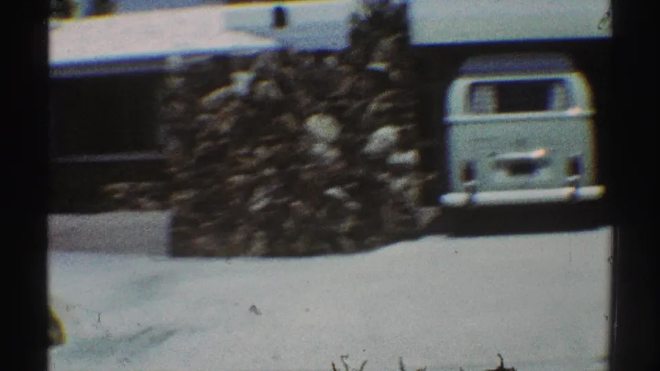 1969 Los Angeles home-movie frame showing a stone wall, driveway, house exterior, and light-colored station wagon.