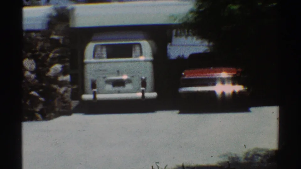 1969 Los Angeles home-movie frame showing a light blue van parked in a garage near a white house exterior.