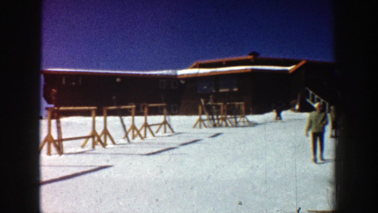 Snowy ski lodge with ski racks and a person walking across the foreground.