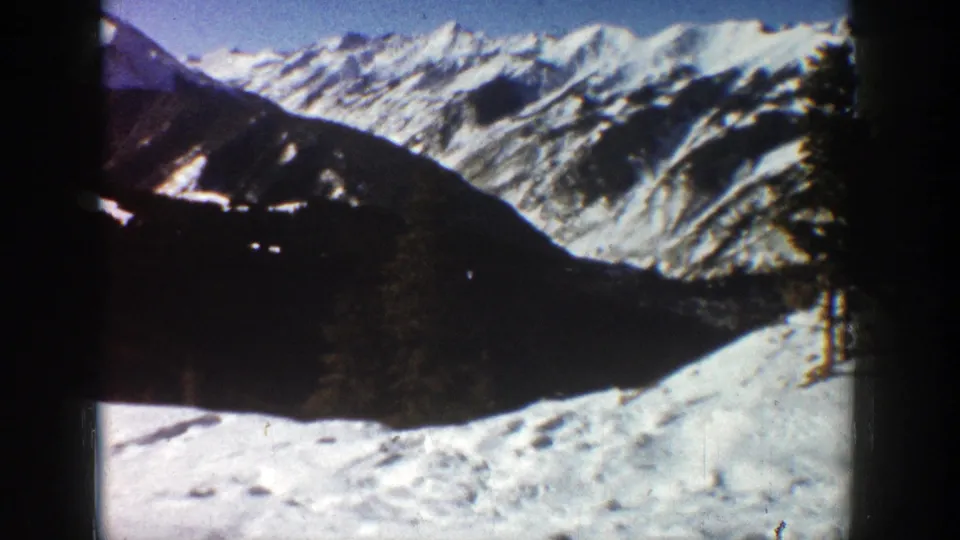 Aspen, Colorado 1961 home-movie frame with snowy peaks, dark mountain face, and bright snow below.