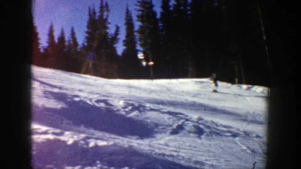 A distant skier descends across an Aspen snow slope in 1961, with evergreen trees and ski tracks visible behind.