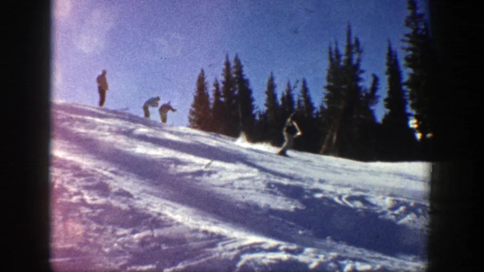 1961 Aspen ski scene with one skier low on the slope and several distant figures above, framed by evergreens and film borders.
