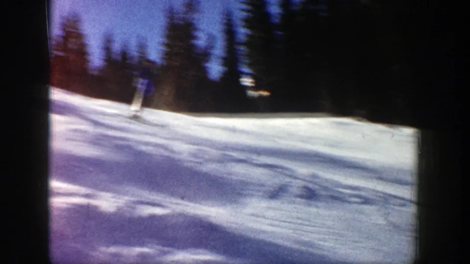 A skier continues downhill on a bright snowfield in Aspen, framed by dark trees and soft 8mm motion blur.