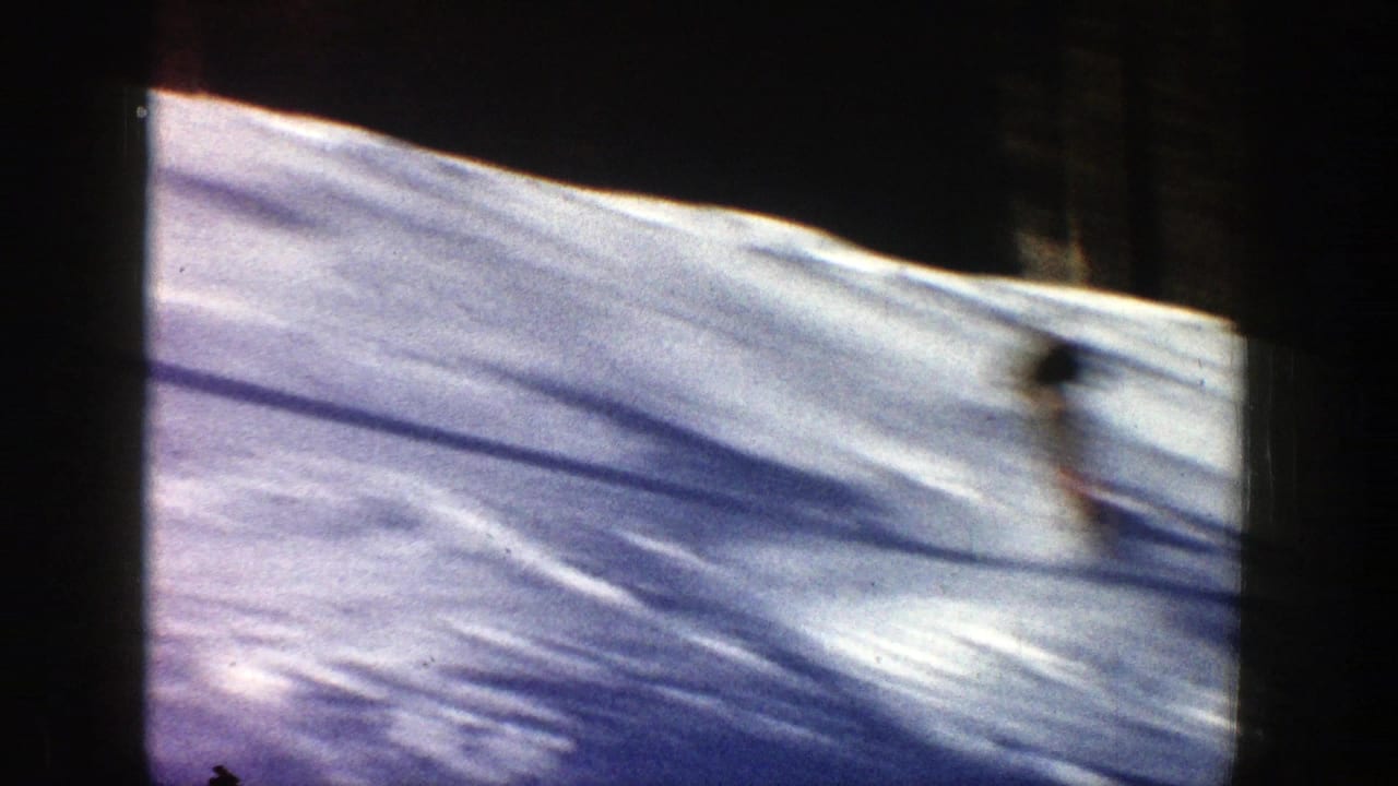Blurred skier moving across a snowy hillside with dark tree shadows.