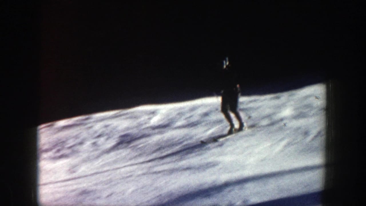 Distant skier moves across a snowy Aspen slope in 1961 home-movie footage, with dark woods and film-frame edges visible.