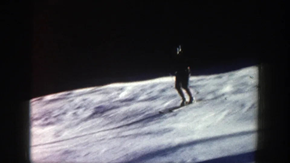 Distant skier moves across a snowy Aspen slope in 1961 home-movie footage, with dark woods and film-frame edges visible.