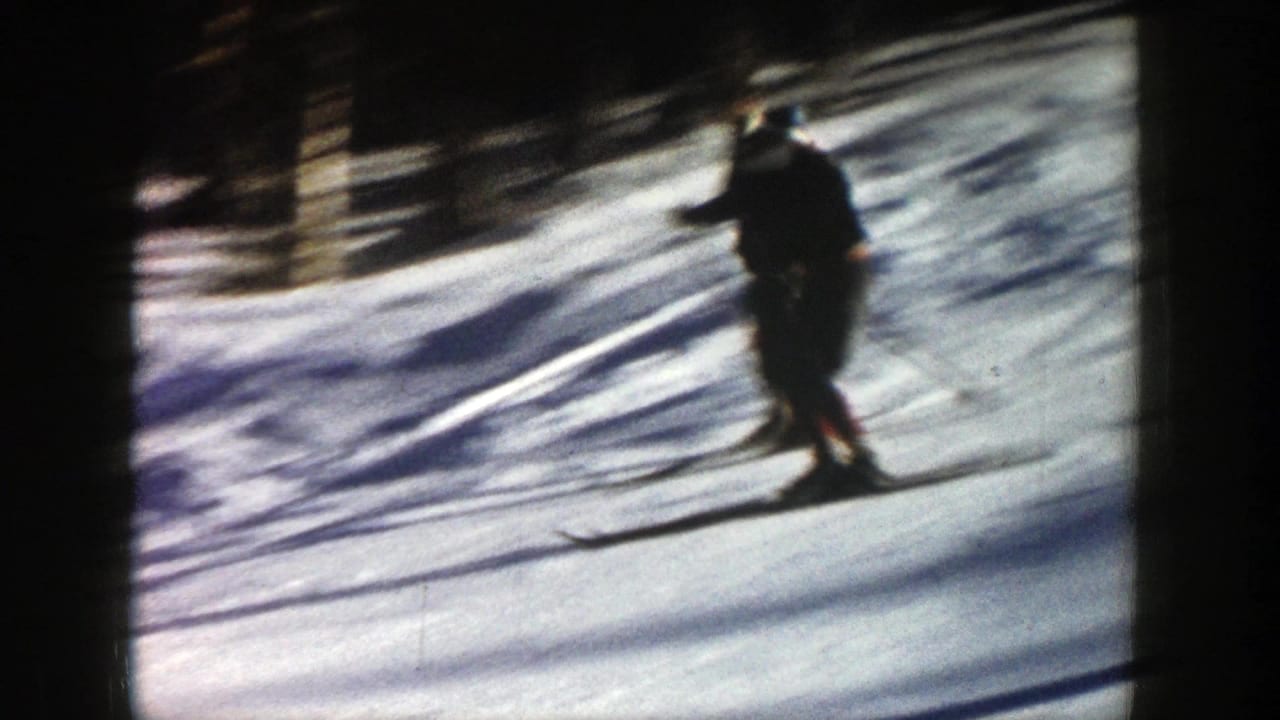 Skier in dark clothing moves downhill across bright snow.