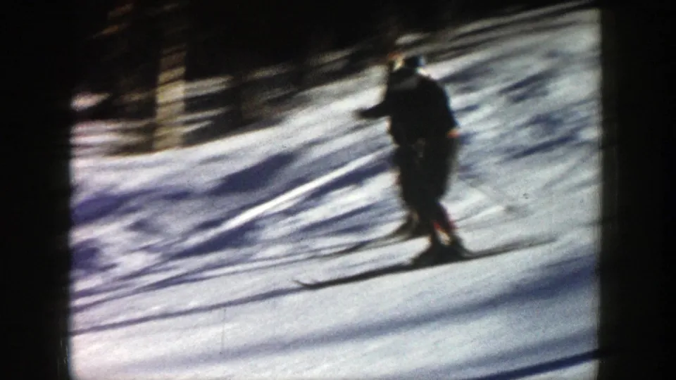 A skier in dark winter clothing descends a bright snowy slope in Aspen, Colorado, with trees and shadows in the background.