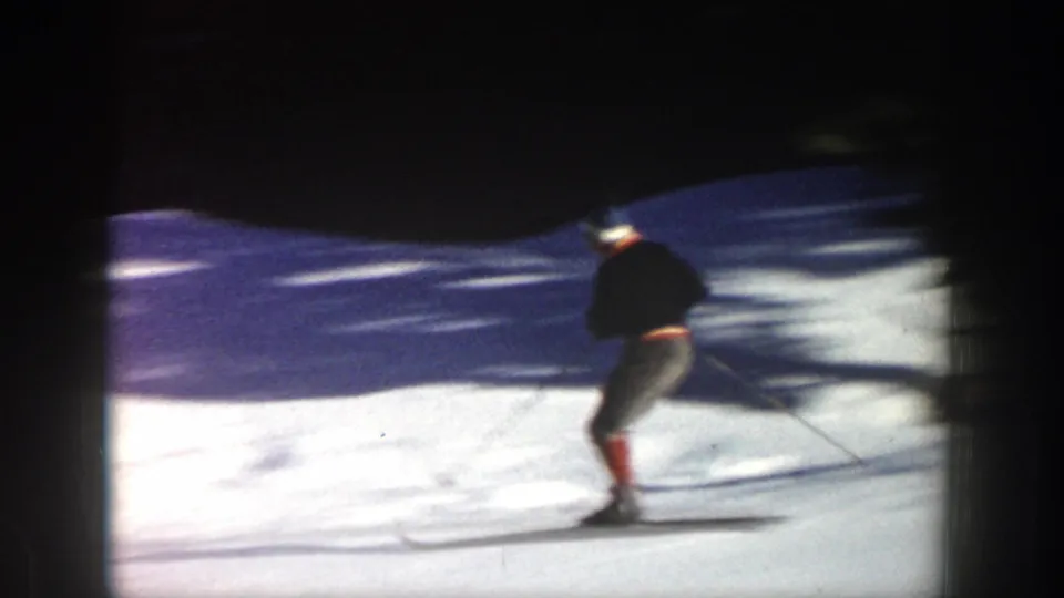 Closer home-movie view of the skier leaning through a turn on an Aspen snow slope, with motion blur and dark framing.