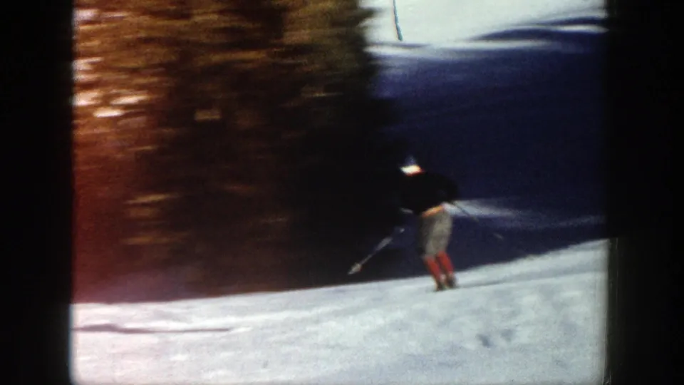 The skier moves away across the Aspen snow near a dark wooded edge, leaving a brief recreational home-movie impression.
