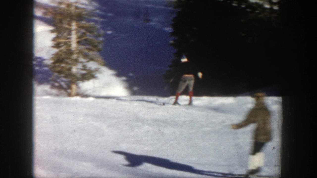 1961 Aspen home-movie frame showing skiers on a bright snowy slope near evergreen trees, with soft 8mm blur and frame borders.