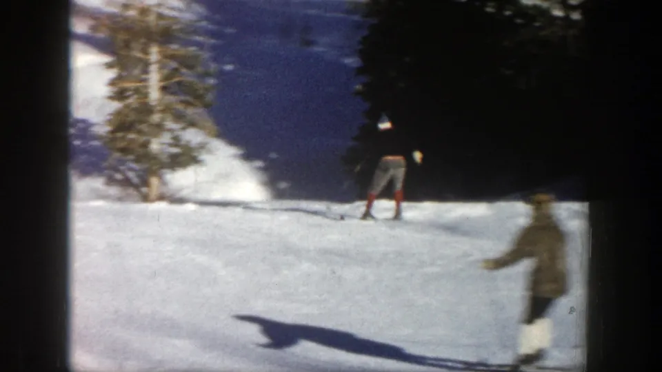 1961 Aspen home-movie frame showing skiers on a bright snowy slope near evergreen trees, with soft 8mm blur and frame borders.