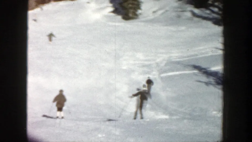 1961 Aspen home-movie frame showing multiple skiers at different distances on a sunlit snowy slope with trees nearby.