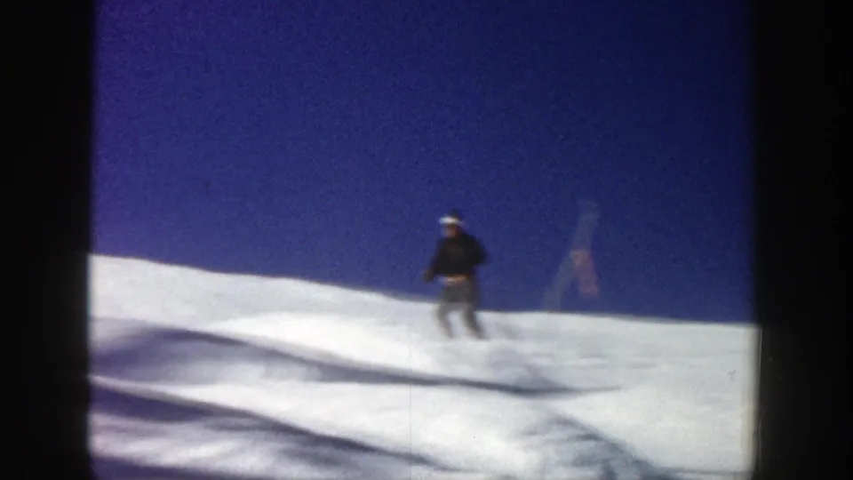 The skier descends across the Aspen snow slope in soft 8mm motion blur, with tracks and a marker visible against the blue sky.
