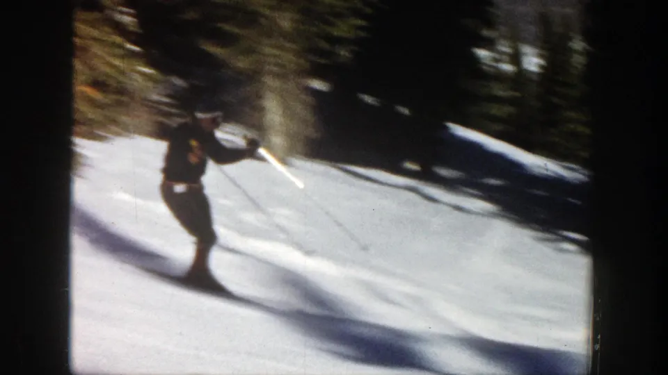 In Aspen, Colorado, 1961 home-movie footage, a skier in dark clothing crosses a snow-covered slope near evergreen trees.