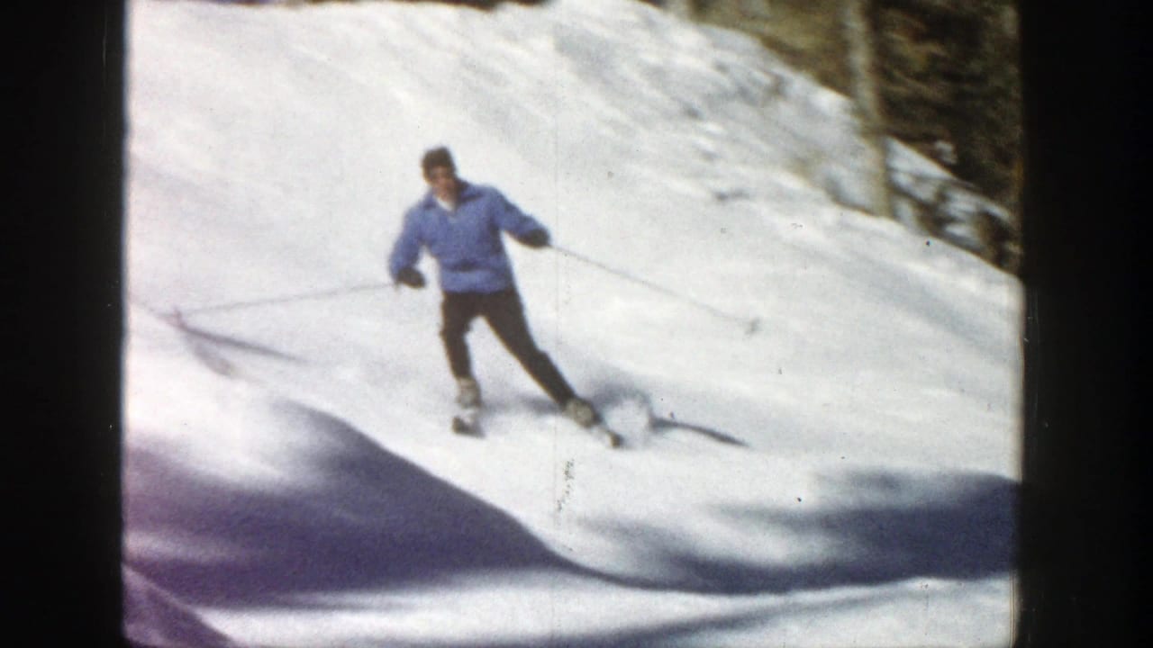 Skier in a blue jacket turns downhill on a snowy slope near trees.