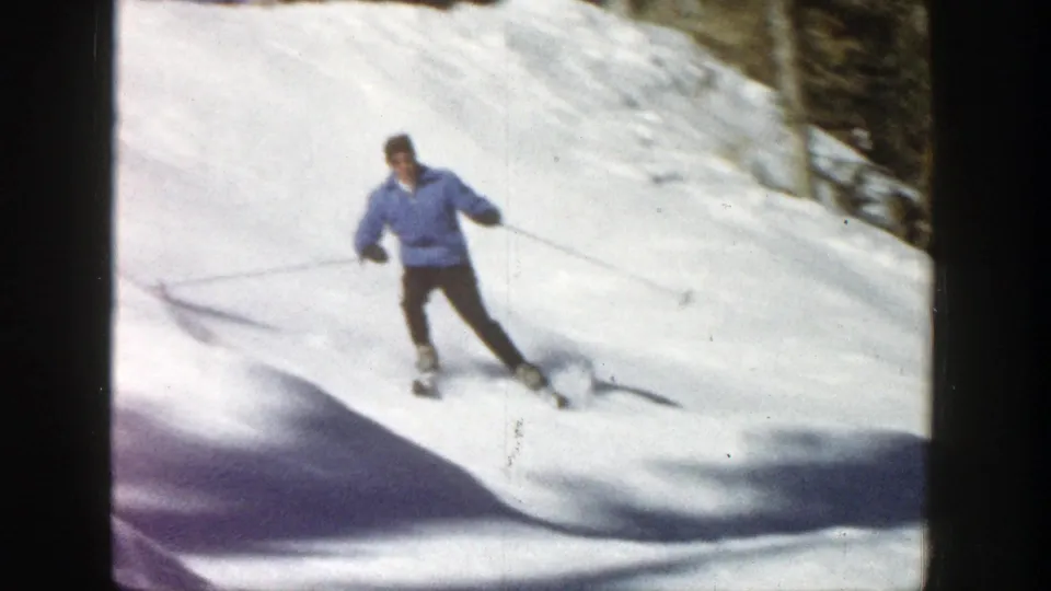 Adult skier in Aspen, Colorado, turns through bright snow with ski poles visible and trees at the edge of frame.