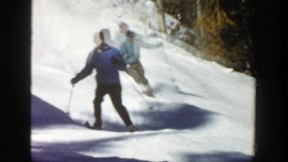 Two adult skiers appear on a snowy Aspen slope, with one in a darker blue jacket closer to the camera.