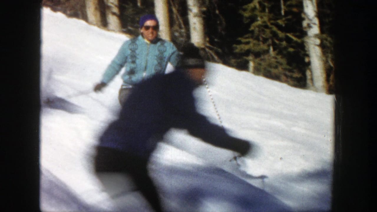 Adult skier in a light blue jacket and purple cap carves across a snowy Aspen slope in 1961 home-movie footage.