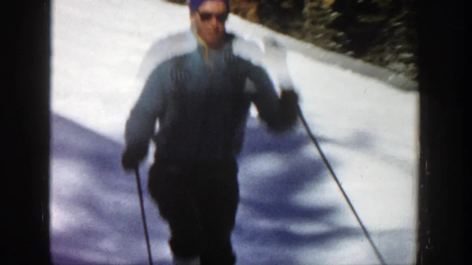 Adult skier moves toward the camera on a snowy Aspen slope, with poles visible and trees in the background.