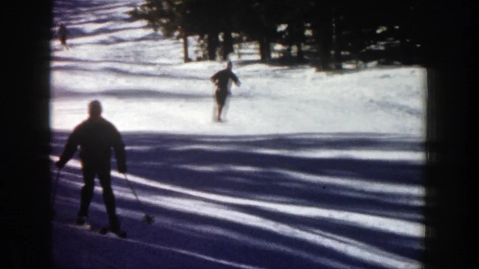 Aspen ski-slope frame showing one skier close to the camera and another descending farther uphill on bright snow.