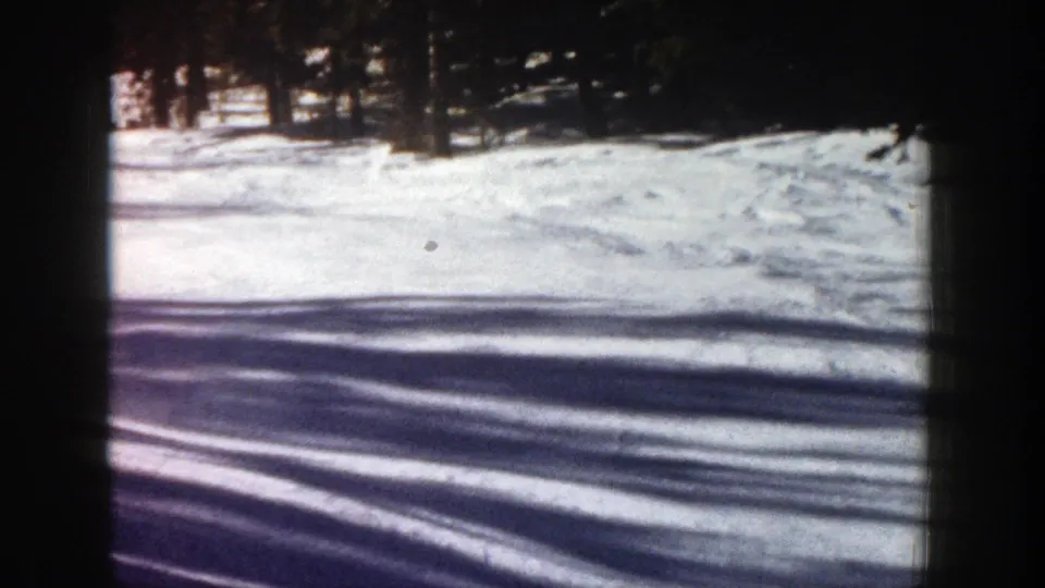 1961 Aspen frame showing a bright snow-covered slope, dark woods at the edge, and strong horizontal shadows across the snow.
