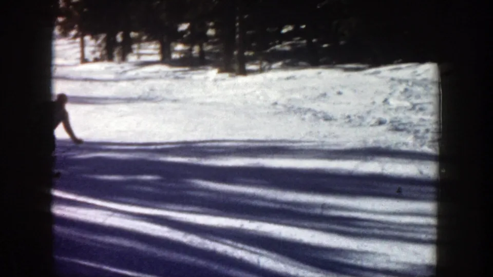 1961 Aspen frame with a partially seen skier near the left edge, crossing a bright snowfield under tree shadows.