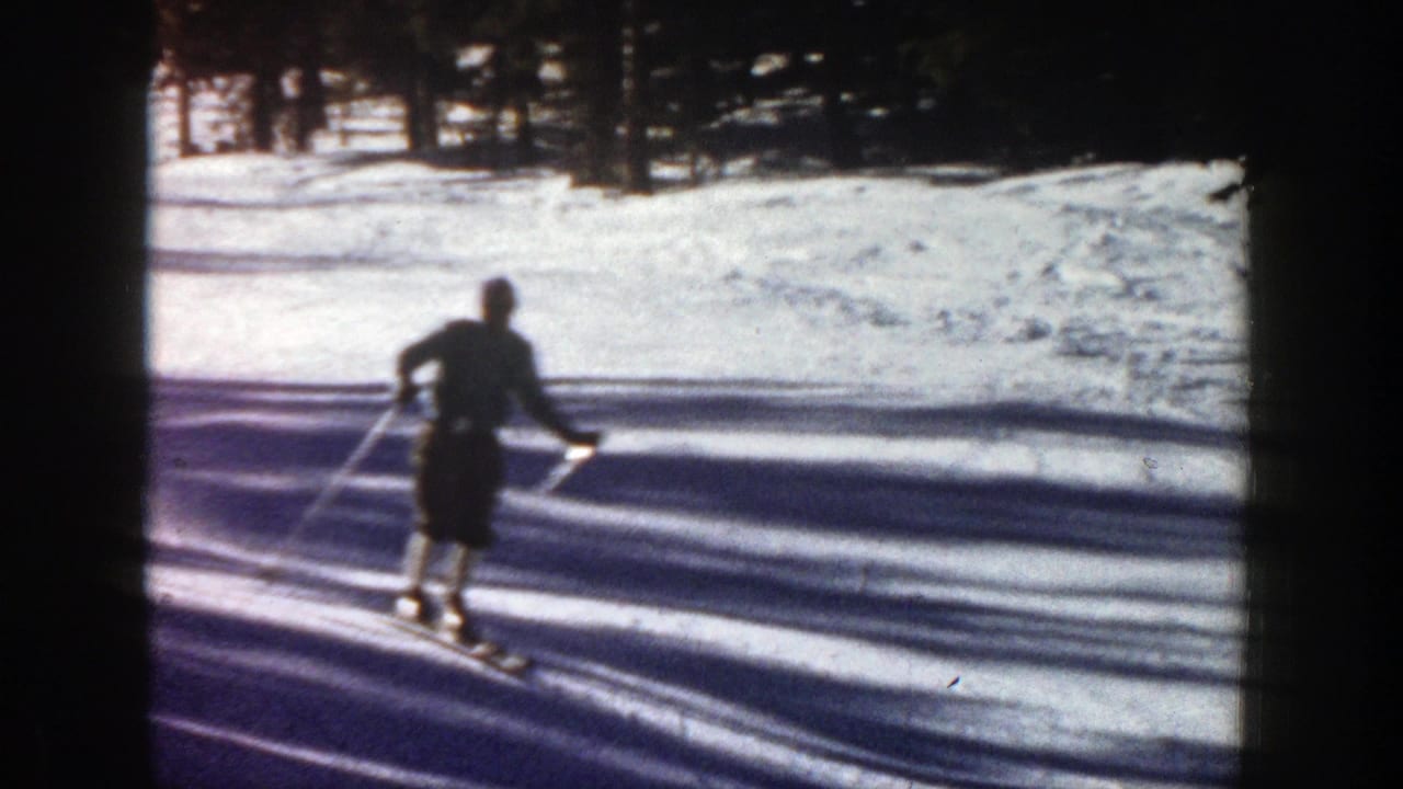A skier in dark winter clothing moves across a bright snowy slope in Aspen, Colorado, in 1961 home-movie footage.