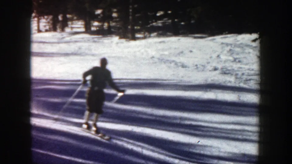 A skier in dark winter clothing moves across a bright snowy slope in Aspen, Colorado, in 1961 home-movie footage.