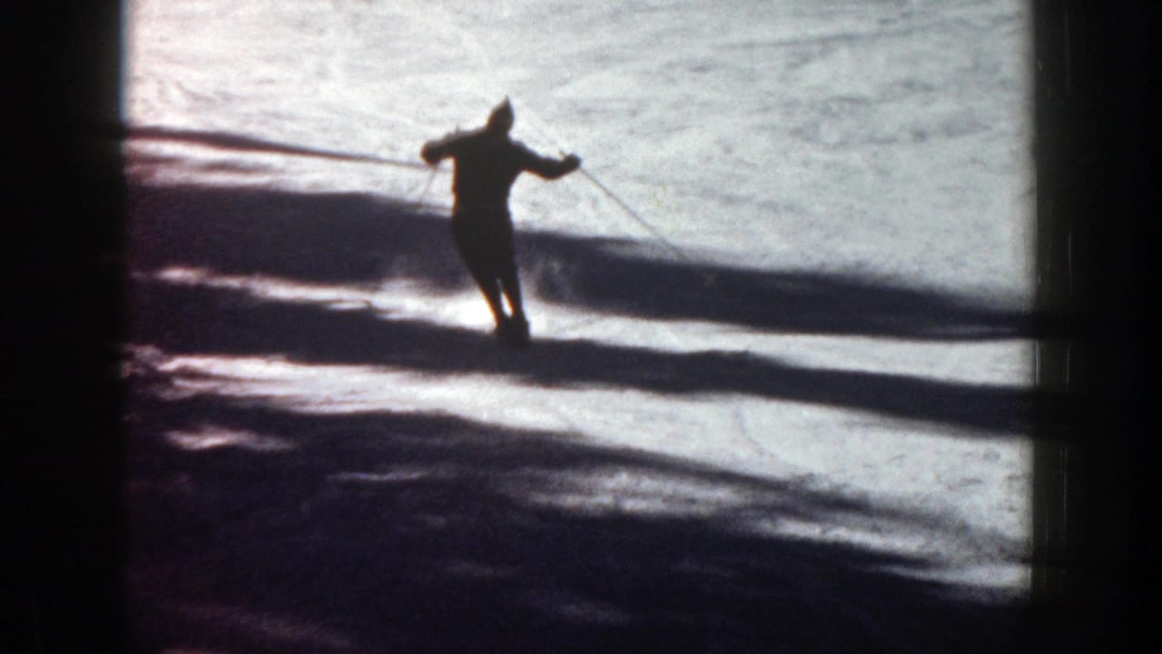 Skier silhouetted on a snowy slope with long shadows across the snow.