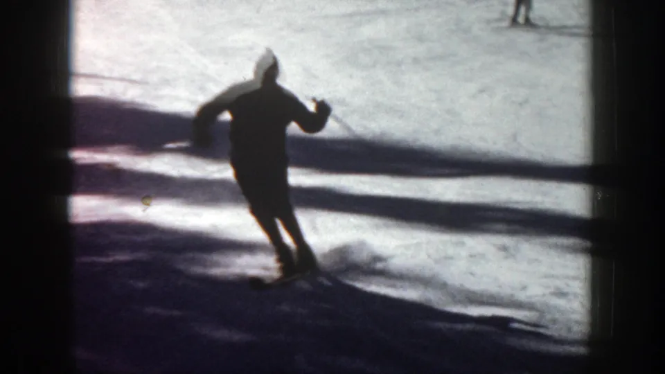 The skier leans into a turn on the Aspen slope, silhouetted against bright snow and a broad shadow line.