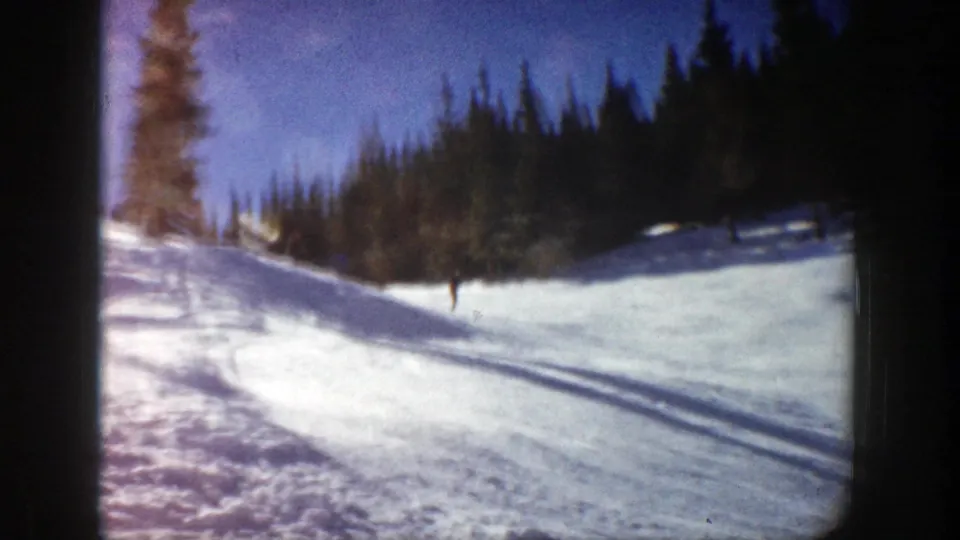 A wider Aspen slope view shows a distant skier below a dark evergreen tree line in 1961 8mm footage.