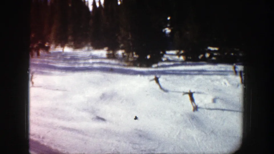 1961 Aspen 8mm frame with two distant skiers moving across sunlit snow, framed by dark trees and visible film edges.