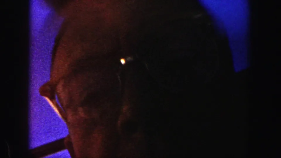 Brief 8mm frame showing a partial adult male face with glasses, likely near the camera between ski-slope shots.