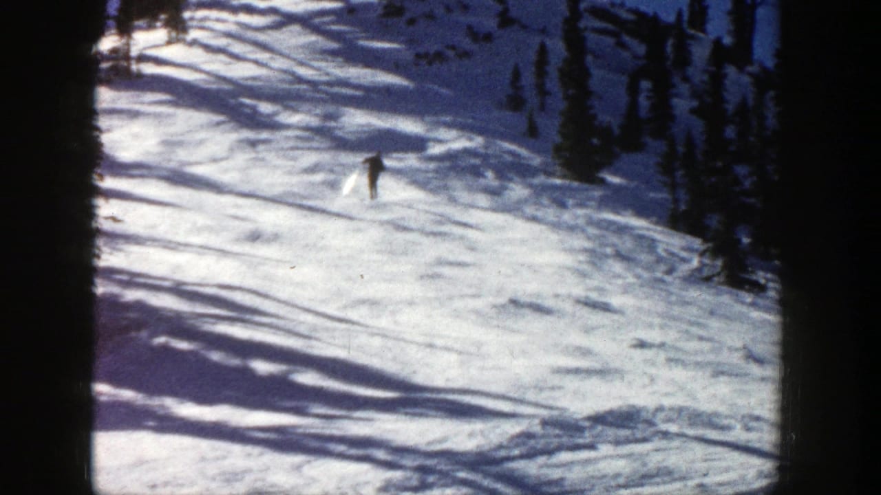 In Aspen, Colorado in 1961, a distant skier moves downhill across sunlit snow with dark evergreen trees nearby.