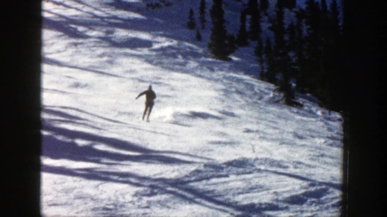 A skier in dark clothing and a blue hat descends a sunny snowy slope in Aspen, Colorado, in 1961 home-movie footage.