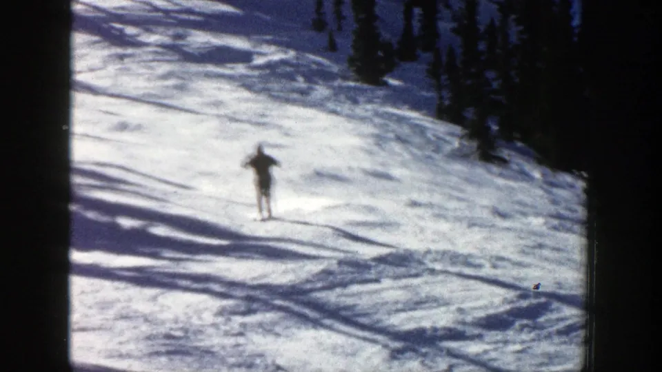 The skier continues downhill across bright Aspen snow, with dark pine trees and long shadows behind them.
