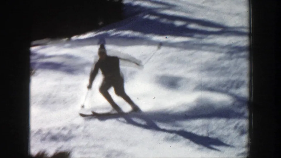 1961 Aspen, Colorado 8mm frame showing a distant skier in dark winter clothing turning across a bright snowy slope.